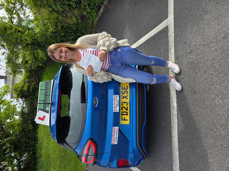 Smiling student with pass certificate next to blue Rev with Kev learner car