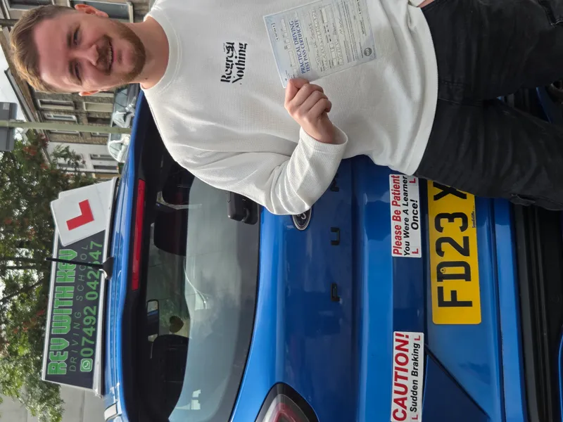 Student celebrating with driving test pass certificate and Rev with Kev car